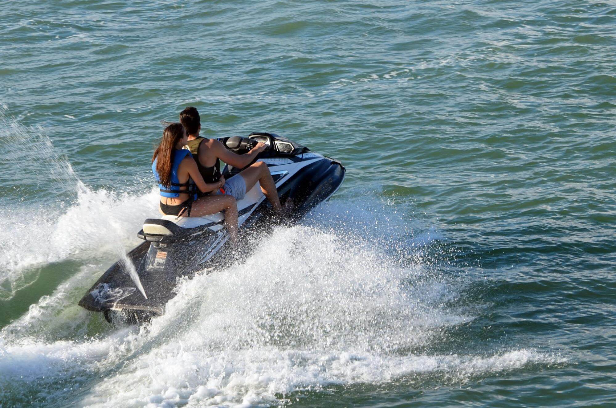 Casal andando de jet ski no mar, criando marolas na água.