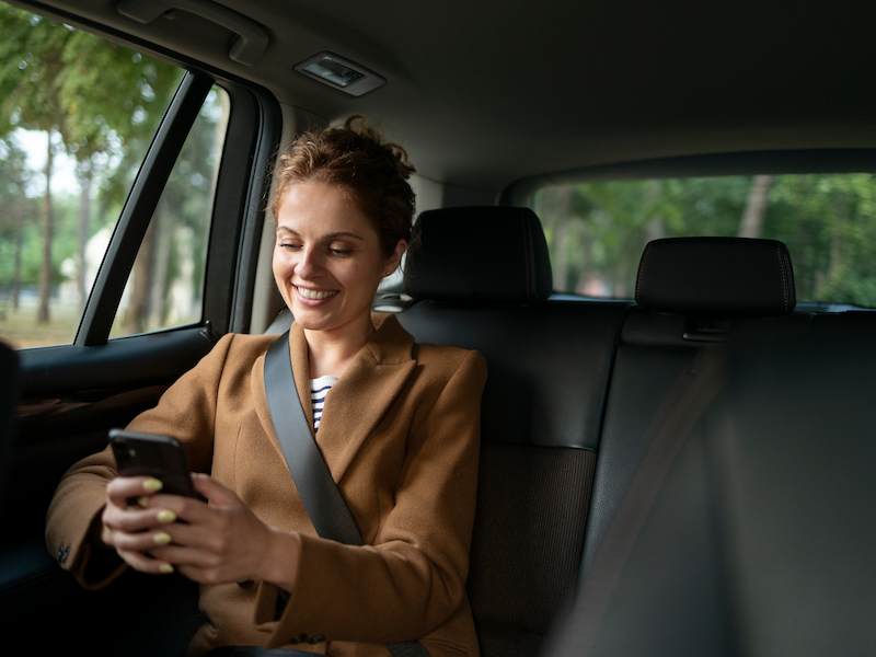Mulher sorridente no banco traseiro do carro usando celular.