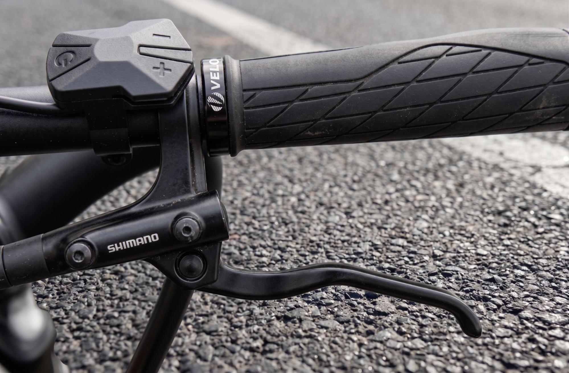 Detalhe do manete de freio Shimano ao lado da manopla e dos botões de controle no guidão de uma bicicleta elétrica. 