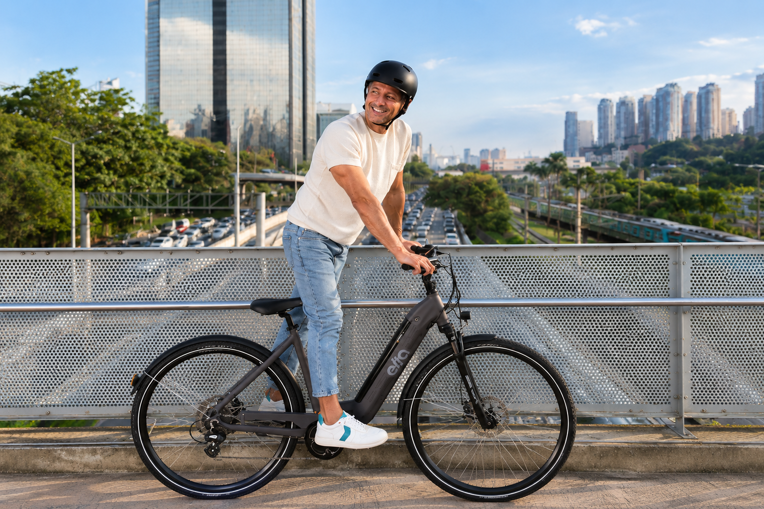 Homem sorrindo, de camiseta branca e calça jeans, apoiado em uma bicicleta urbana elétrica preta sobre uma passarela.