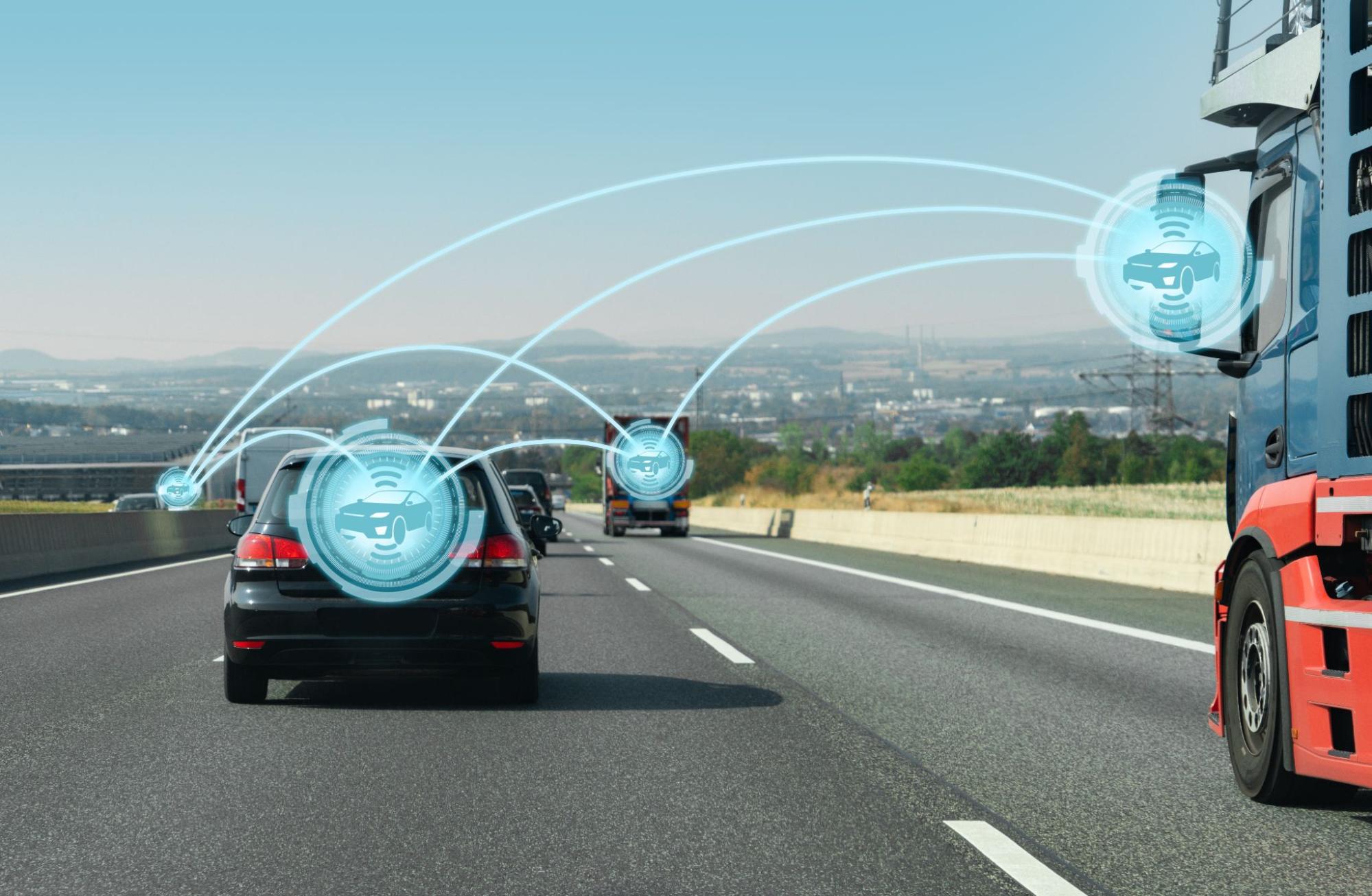 Carros e um caminhão circulando numa autoestrada, interligados por linhas virtuais e ícones azuis que representam conectividade e tecnologia autónoma.