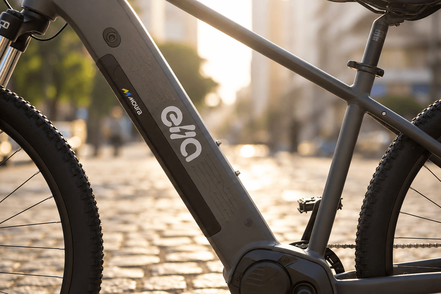 Bicicleta elétrica Ella, a bike elétrica da Moura, na cor cinza, ao entardecer em rua de paralelepípedo