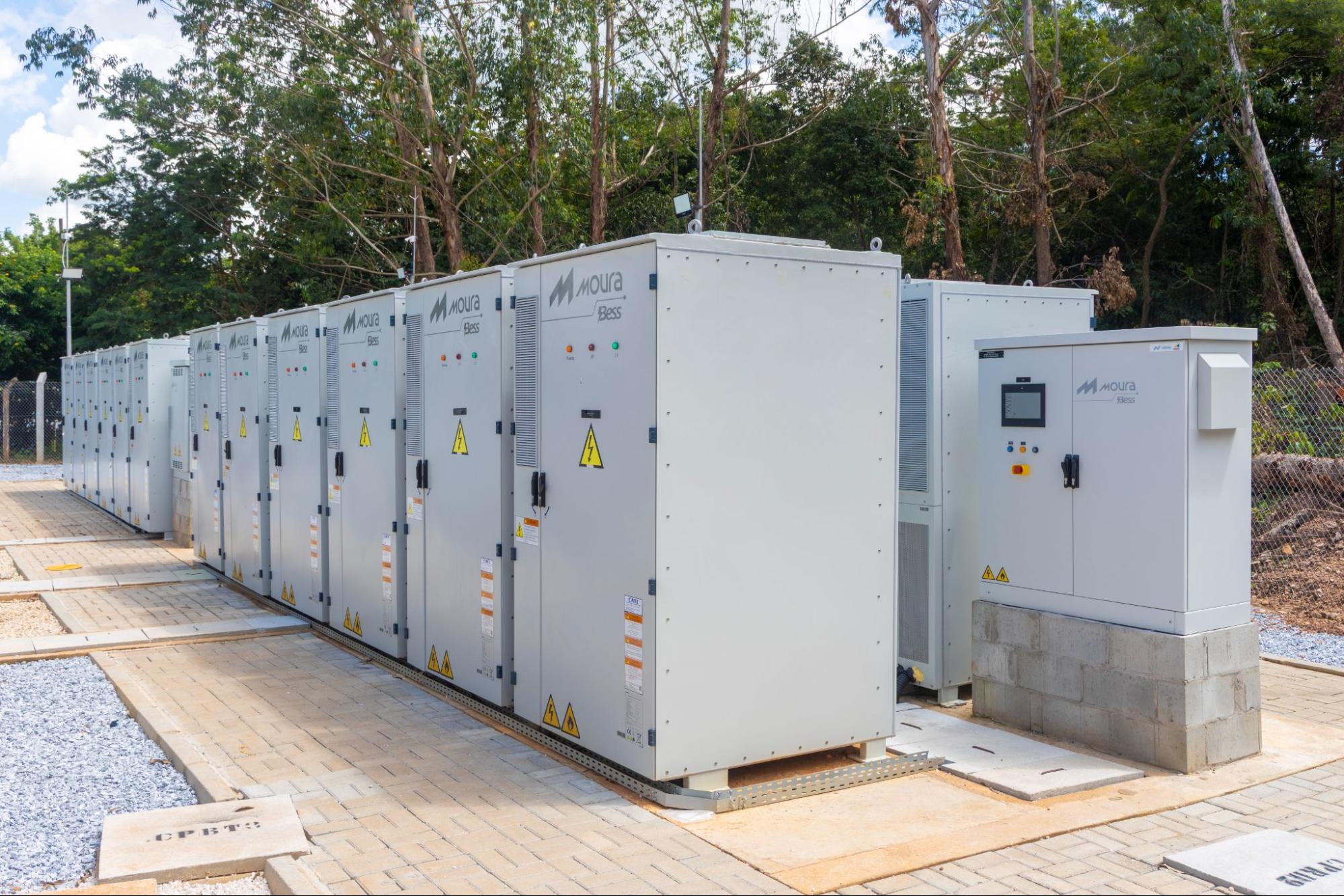 Fileira de armários brancos do sistema de armazenamento de energia em baterias Moura BESS instalados ao ar livre.