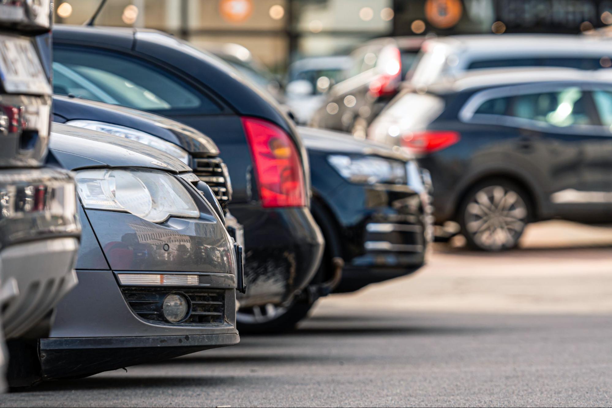 Fila de automóveis modernos estacionados lado a lado num parque de estacionamento ao ar livre.   